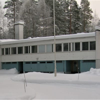 Matala, tiiliverhoiltu rakennus metsän reunassa.