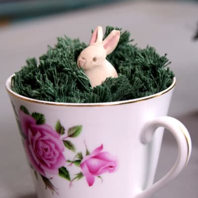 En kaffekopp med grönt garn och en kanin i garngräset