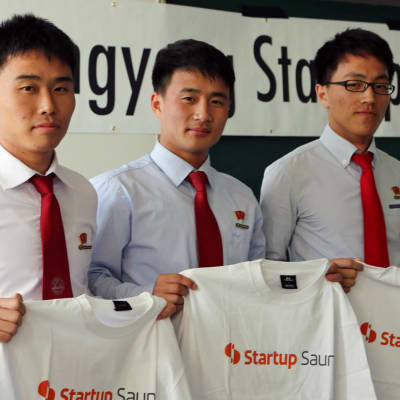 Startup Sauna Pohjois-Koreassa. Opiskelijat ovat pukeutuneet vaaleisiin kauluspaitoihin ja punaisiin kravatteihin. Kaikilla heistä on samantyyppiset lyhyet hiukset. 