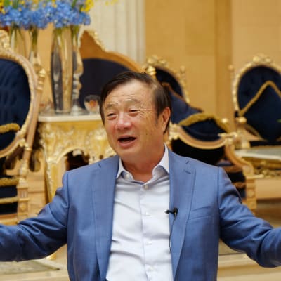 Ren Zhengfei, här iklädd blå kostym. I bakgrunden förgyllda stolar.