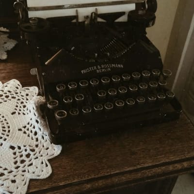 En gammaldags skrivmaskin på en mörk byrå med en vit bordsduk bredvid. 
