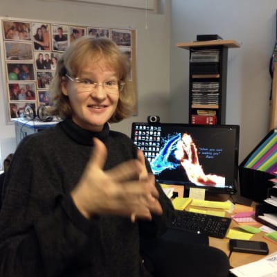 en kvinna sitter framför en dator och gör en rörelse med händerna på teckenspråk