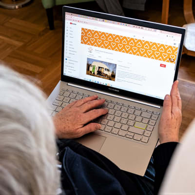 Vanhus istuu nojatuolissa kannettava tietokone sylissään ja kädet näppäimistöllä.