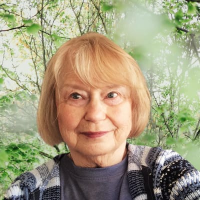 Stina småler in i kameran mot en grönskande bakgrund.