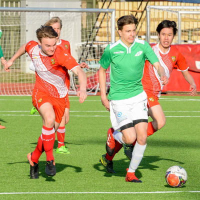 En fotbollsspelare springer med bollen i fötterna medan några spelare jagar honom.