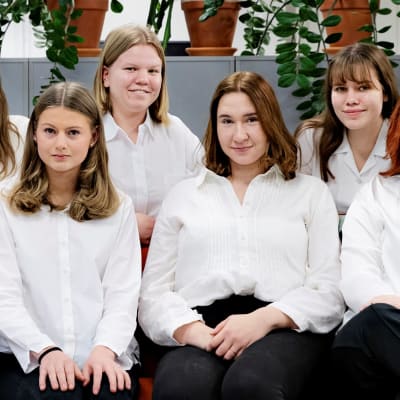 Sju unga kvinnor med vita skjortor och svarta byxor.