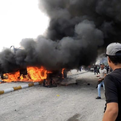 Demonstranter samlas kring ett brinnande militärfordon i Nasiriyah, Irak.