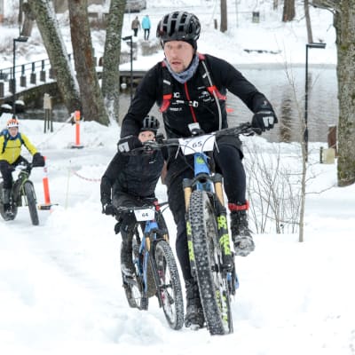 Tomi Paavola cyklar i vinterräng upp för en backe.