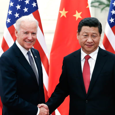 Joe Biden och Xi Jinping skakar hand. I bakgrunden USA:s och Kinas flagga.