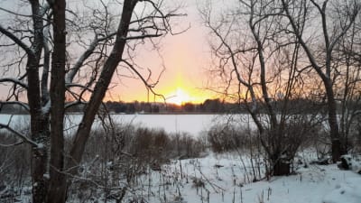 Ett vinterlandskap och en tidig solnedgång över en frusen insjö.