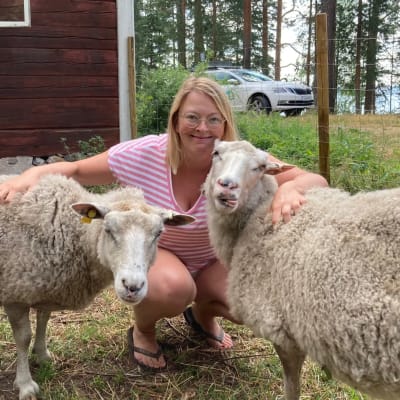 Nainen kyykistyneenä lampaiden kanssa.