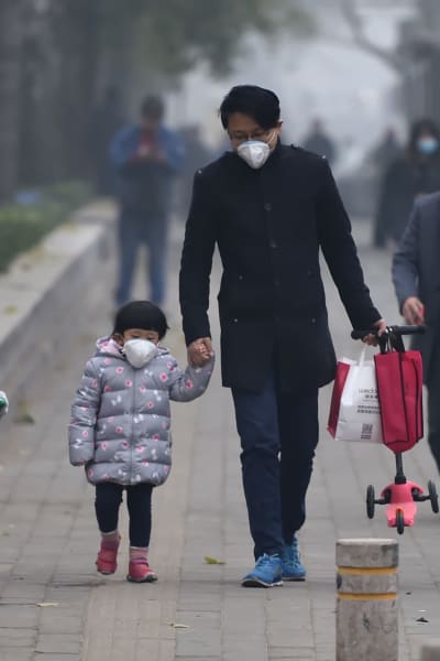 En kinesisk pappa och dotter har på sig ansiktsmasker när de promenerar i luftförorenade Peking.