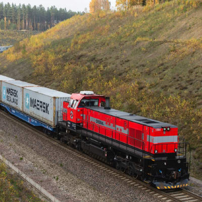 Ett rött lokomotiv med gråa vagna med Maersks logotyp. 