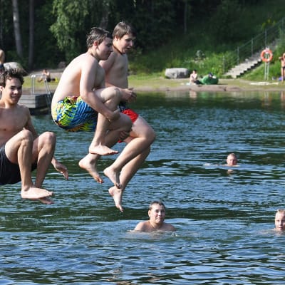 Pojat hyppäävät laiturilta veteen.