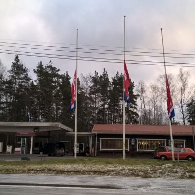 En bränslemack och tillhörande kafébyggnad, Teboil-flaggor i halvstång.