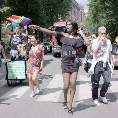 Kelet går mitt i ett Pridetåg i Helsingfors och håller i prideflaggan.