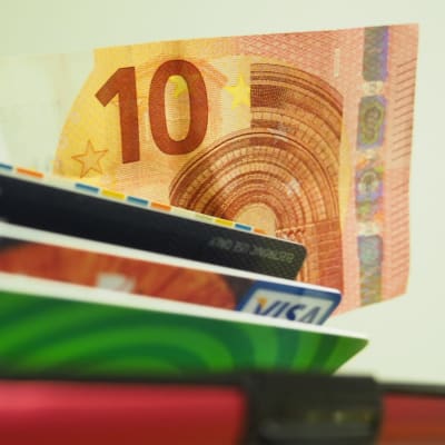 En tioeurossedel kommer fram ur en plånbok. Ett busskort och bankkort syns också delvis.