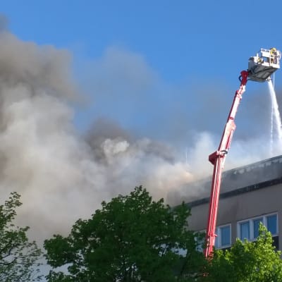 Palokunnan nostokurjesta ruiskutetaan vettä savuavaan rakennukseen.
