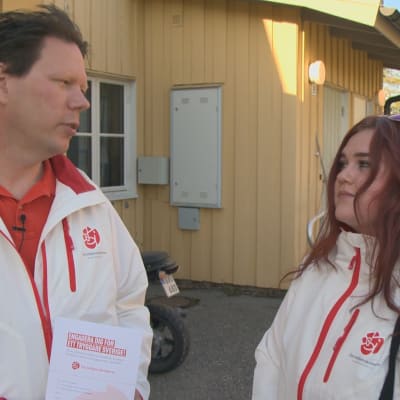 Två personer i vita rockar med Socialdemokraternas logo i ett bostadsområde.