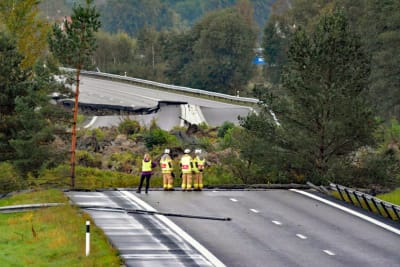 Tre brandmän och en kvinna står och inspekterar en väg som rasat.