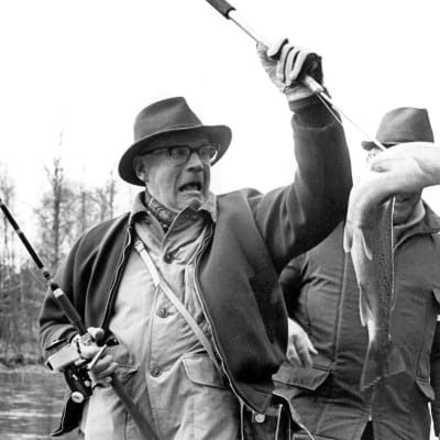 Urho Kekkonen painii kalan kanssa hämmästynyt ilme kasvoillaan.