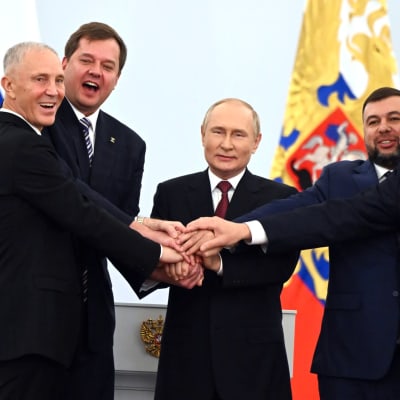 Rysslands president Vladmir Putin och fyra andra män håller varandra i händerna och firar att Ryssland annekterar delar av Ukraina.