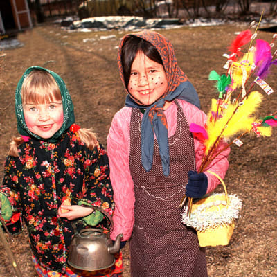 Kaksi iloista tyttöä pääsiäisnoitina virpomassa.