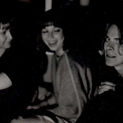 Mustavalkoinen kuva jossa kaksi naista ja yksi mies istumassa melko lähekkäin. Mies katsoo kameraan, toinen naisista nauraa.