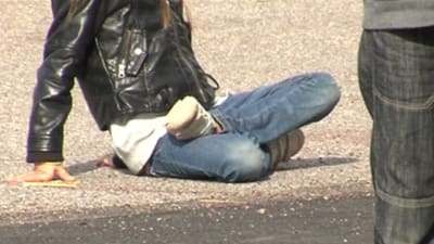 Ungdom sitter ute på marken medan en annan står bredvid.