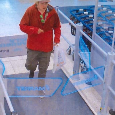 En man i röd blus och skärmmössa som går i en mataffär. Polisens foto på en misstänkt rånare i Karis.