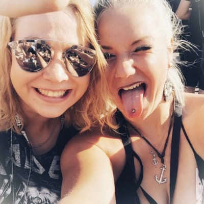 Kaksi nuorta naista katsoo kameraan. Vasemman puoleisella naisella peilipintaiset aurinkolasit ja Iron Maiden -bändipaita. Oikean puoleinen nainen virnistää kieli ulkona. Hänellä on kielikoru.