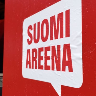 Suomi areena juliste läheltä, taustalla näkyy kaksi ihmistä lavalla.