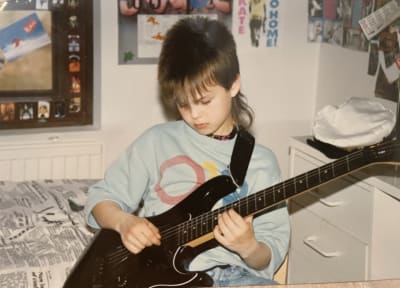 Nuori poika soittaa sängynreunalla kitaraa.