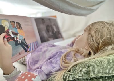 En liten flicka läser en bilderbok liggandes ner med huvudet på en dyna.
