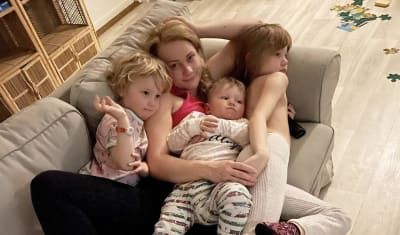 Trebarnsmamman Carola Nordberg ligger i soffan med alla tre barn i famnen. Carola är vänd mot kameran med ett uppgivet ansiktsuttryck.