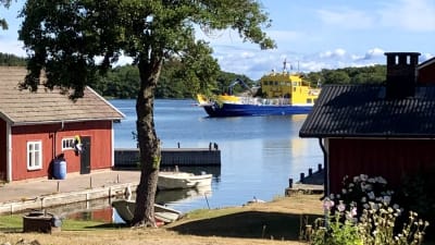 Förbindelsefartyget anländer tll Lökholm, med bryggor och sjöbodar i förgrunden.