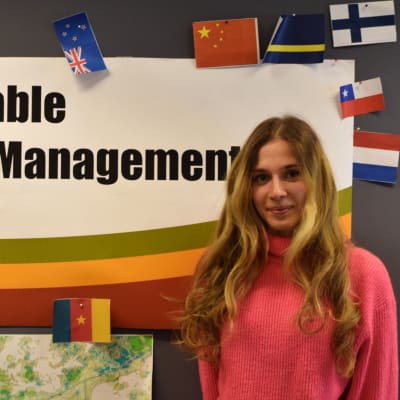 En ung kvinna framför en poster där det står Sustainable Coastal Management. Runt postern finns det flaggor från flera olika länder.