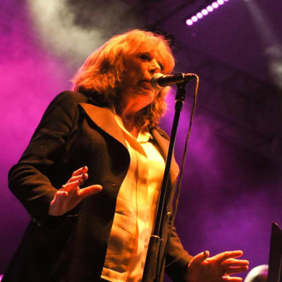 Marianne Faithfull sjunger i en mikrofon som är i en mikrofonställning och hon har ett notställ framför sig.