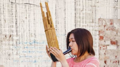 Nainen soittaa puisista putkista rakennettua suu-urkusoitinta