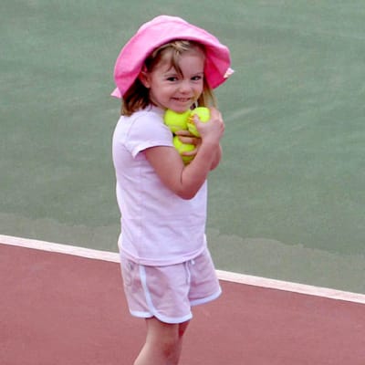 En liten flicka står på en tennisplan med tennisbollar i famnen. Hon är klädd helt i ljusrött med en ljusröd hatt på huvudet.