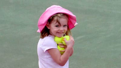 En liten flicka står på en tennisplan med tennisbollar i famnen. Hon är klädd helt i ljusrött med en ljusröd hatt på huvudet.