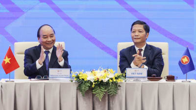 Två vietnamesiska män sitter vid ett bord och klappar. Vietnams premiärminister Nguyen Xuan Phuc (vänster) och handels- och industriminister Tran Tuan Anh i en virtuell signeringsceremoni.