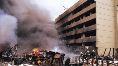 Efter attackerna i Nairobi 1998. Ett bombaderat hus med bilskrot som exploderat framför sig. Ett rökmoln och brandmän som släcker elden 