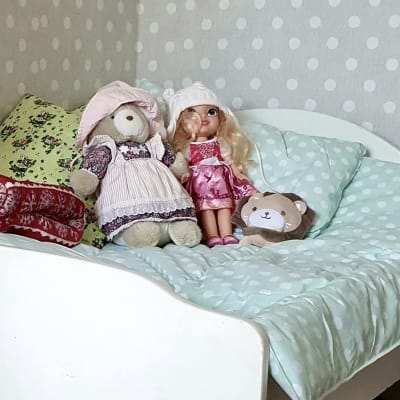 En bäddad säng med en docka, en nalle och ett mjukt lejon placerade på mitten på ett harmoniskt sätt.