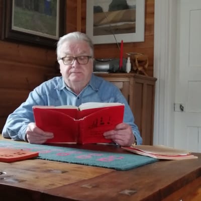 Mies lukee punaista kirjaa pöydän ääressä.