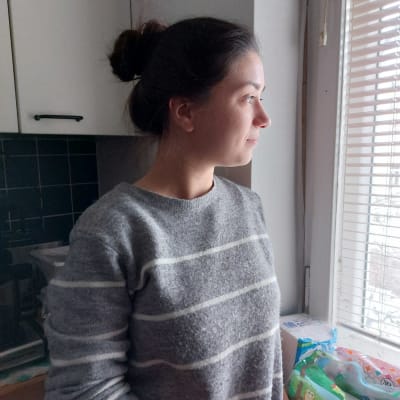 En ung kvinna står i centrala Borgå och tittar ut genom ett köksfönster.