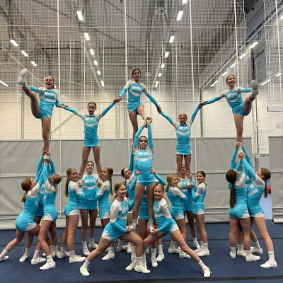 Kouluikäisten tyttöjen cheerleading-joukkue on tehnyt kuvassa pyramidin. Joukkueen jäsenillä on päällään yhtenevät sini-valkeat kisa-asut.