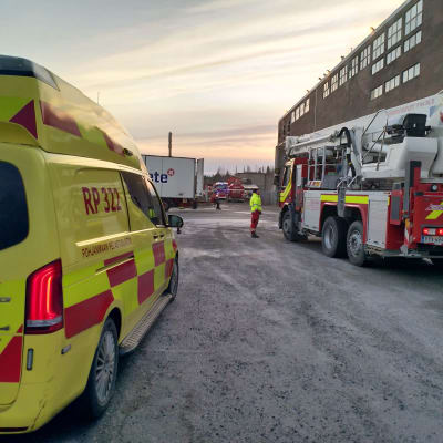 En ambulans och en brandbil står parkerade på gården till en industrihall.