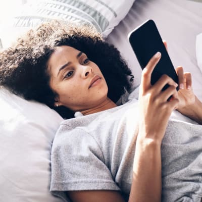 Kvinna ligger på en säng och tittar på sin telefon
