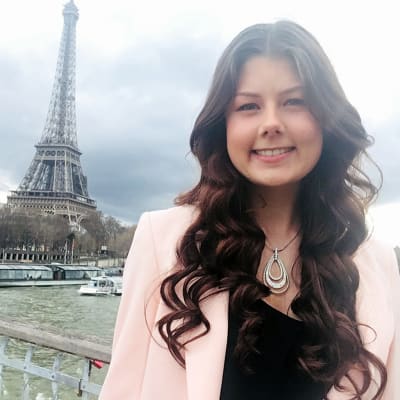 En kvinna med långt brunt hår som befinner sig i Paris. I bakgrunden syns Eiffeltornet. 